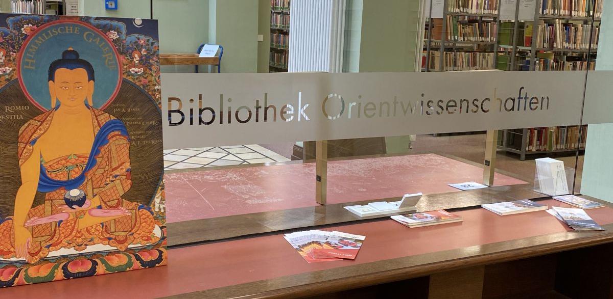 enlarge the image: Illustrated book with Buddhist art on a table in the entrance area next to the lettering Bibliothek Orientwissenschaften, 2020, Photo: Franz Xaver Erhard