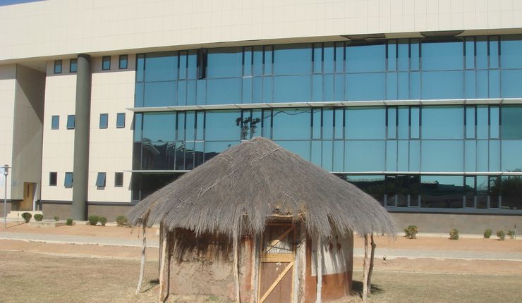 A thatch-roofed round hut directly in front of the Chinese-built glass block that is the Faculty of Business at the University of Botswana in Gaborone.
