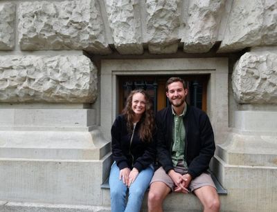 Two smiling students are sitting in front of the Albertina library.