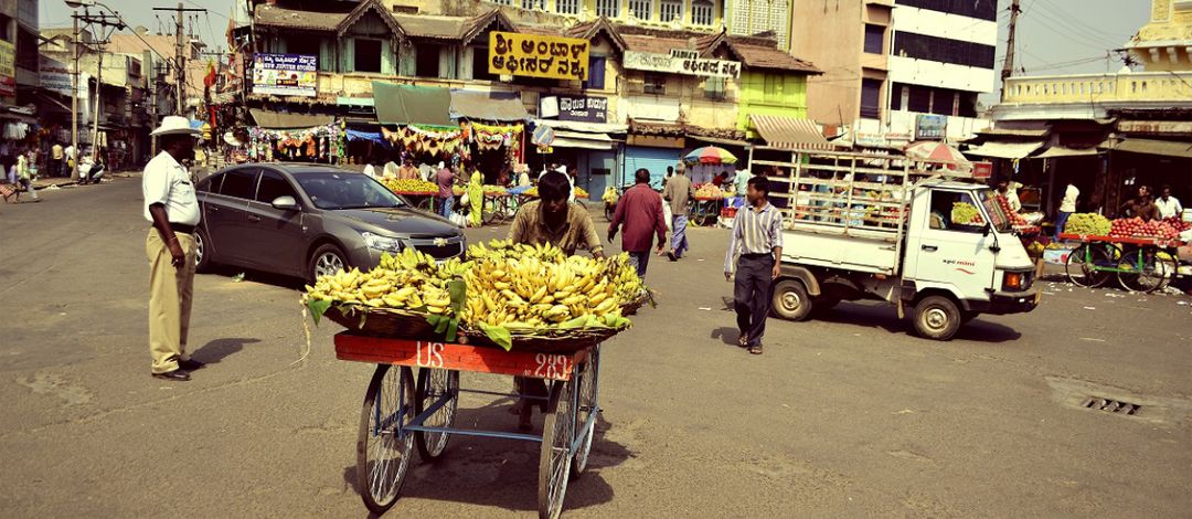 Auf einem kleinen Martkplatz schiebt ein Mann einen Wagen mit Bananen