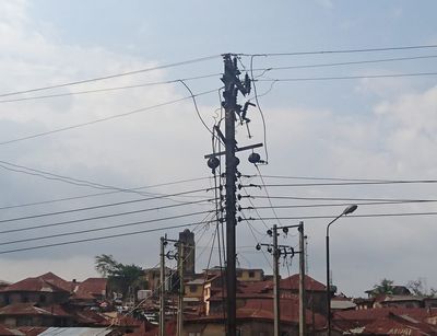 Electricity pole and cables photographed from below against the background of an urban neighbourhood in Ibadan, Nigeria.