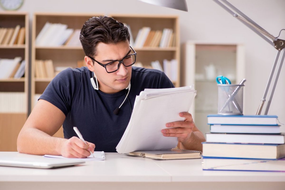 enlarge the image: Ein Student sitzt an seinem Schreibtisch und studiert konzentriert seine Unterlagen.