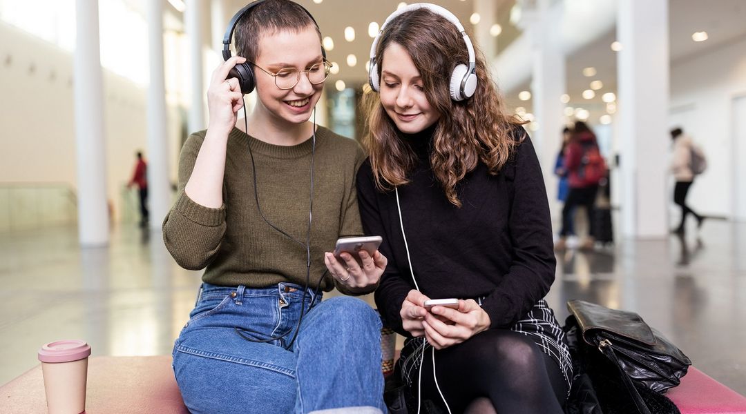 Zwei STudentinnen sitzen nebeneinander und hören etwas mit Kopfhörern