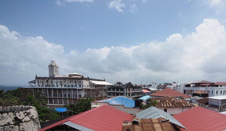A bird's eye view of the roofs of Zanzibar Stone Town, showing roofs made of different materials from brown, rusty corrogated iron to new, read, shiny plastic roofs.