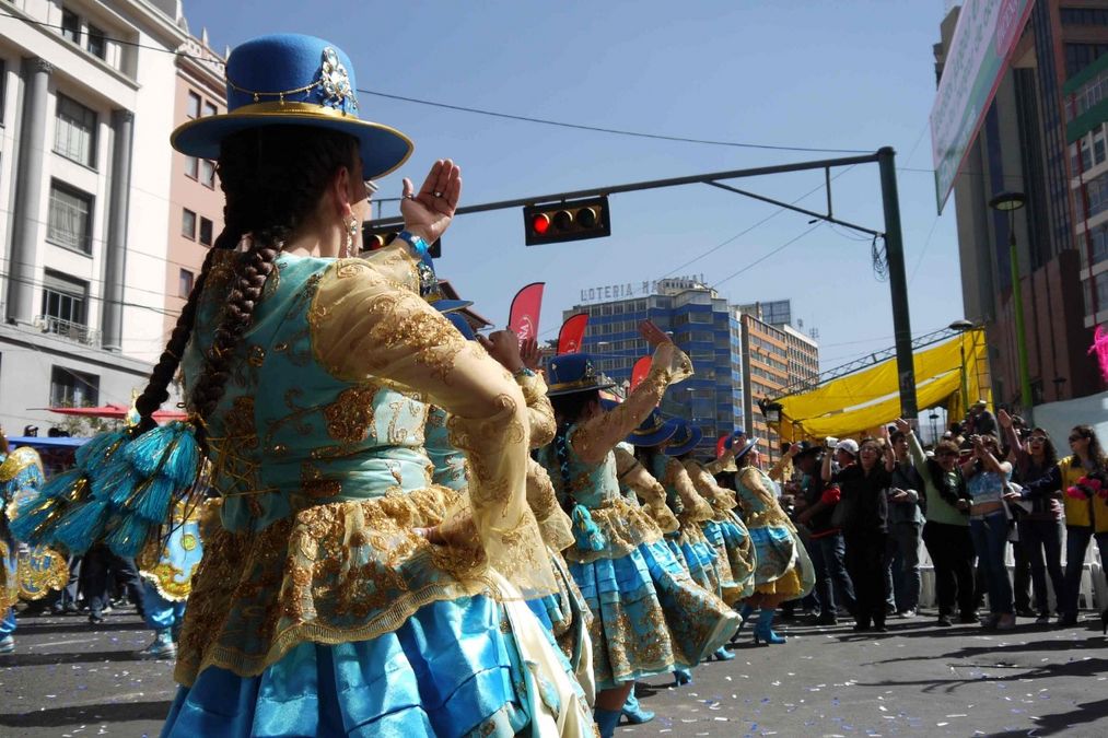 enlarge the image: Tänzerinnen in gold-blauen Kleidern und Hüten auf einem Straßenumzug grüßen das Publikum